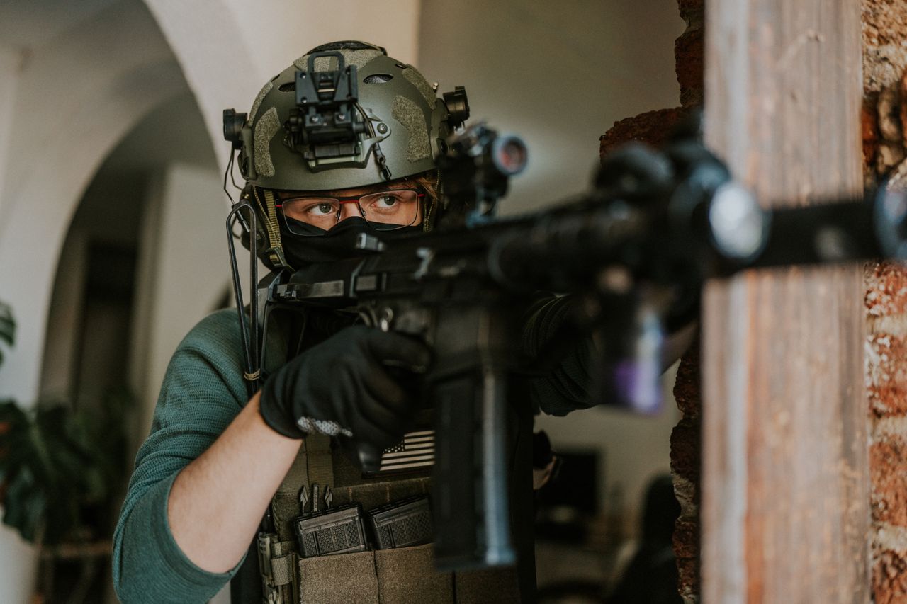 A soldier in tactical gear aiming a rifle indoors, focused and ready in a high-stakes scenario.